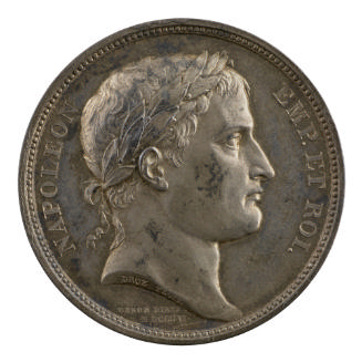 Silver medal of a man in profile to the right with short hair and a laureate