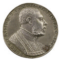 Silver medal of a man wearing a pleated shirt, several chains around his neck and an embroidere…