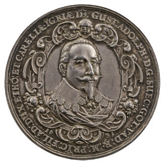 Silver medal of a man with a mustache and goatee, wearing a mantle and large collar