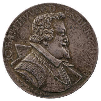 Silver medal of a man in profile to the right wearing a mantel on his left shoulder and a medal…