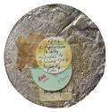 Unmarked tin reverse of a medal with three stickers taped to it: on top, a white, round sticker…