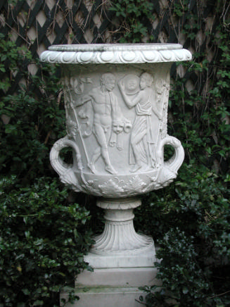 A large white marble garden vase surrounded by green shrubs
