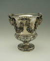 Silver wine cooler with intricate plant designs and rams' heads