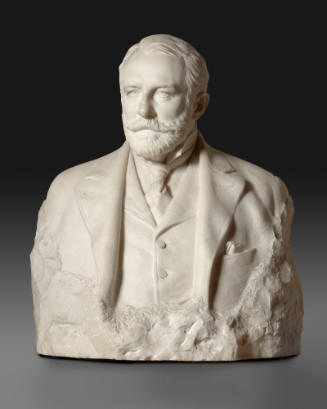 A marble bust of Henry Clay Frick.  He is looking to his right and is bearded. He wears a suit …