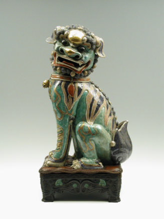 Green porcelain lion with gold, black, and red stylized markings, seated on hind legs, on a bla…