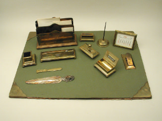 Green blotter with letter opener, brass boxes, calendar, letter holder, and other desk accessor…