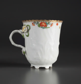 White teacup with red flowers and greenery painted at the top, a ceramic flower is above the ha…