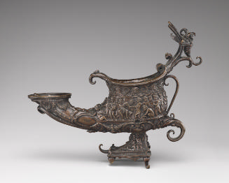 A bronze lamp that is shaped like a shoe and rests on a pyramidal base.  It is covered with int…