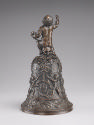 The back view of a bronze hand bell. The body of the hand bell is decorated with lively motifs,…