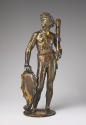 Bronze sculpture of a man standing upright.  His head is turned to his right and he is holding …