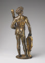 Back view of a bronze sculpture of a man standing upright.  His head is turned to his right and…