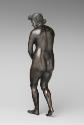 Back view of a bronze sculpture of a naked female figure. Her face has a look of shock on it, h…