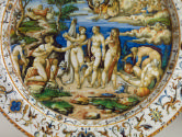 Detail of the center of the dish depicting a scene populated by male and female nude standign a…
