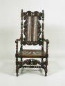 Front view of walnut armchair with scrollwork decoration and woven seat
