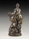 Back view of a bronze sculpture of Triton and Nereid.  Triton is straddling a conch shell and l…