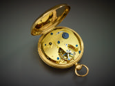 Reverse side of pocket watch showing open lid and movement all in gold, gilt brass and blued st…