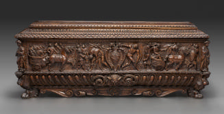 Front view of wooden chest with high relief carving and coat of arms in the center