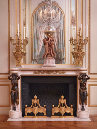 Chimneypiece with two bronze female figures on either side and gilt firedogs in the middle. A c…