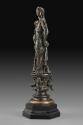Side view of a bronze sculpture of a female figure with a cornucopia.  Her head is turned to he…