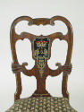 View of back of walnut frame chair with crest and upholstered seat , showing crest