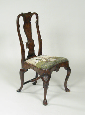 Walnut frame chair with needlepoint upholstered seat with woman standing outdoors