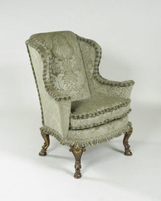 Side view of winged armchair upholstered in light green silk with a damasque motif