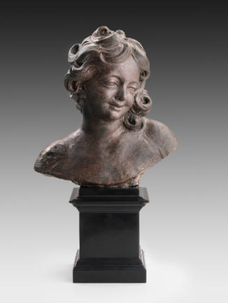 Terracotta sculpture of a head of an angel.  The angel has curly hair, which gathers by the lef…