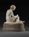 Back view of a marble sculpture of Friendship.  She is sitting down with her legs stretched out…