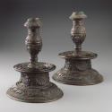 View of the pair of bronze candlesticks featuring intricate motifs throughout.