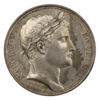 Silver medal of a man in profile to the right with short hair and a laureate