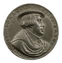 Silver medal of a man with mid length hair wearing a low hat, high collar, cloak and chain
