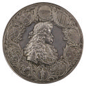 Silver medal of a man with a mustache wearing a wig, armor, and a sash and surrounded by foliag…