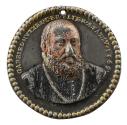 Polychrome lead medal of a man with short hair, a mustache and a beard, wearing a coat and chai…