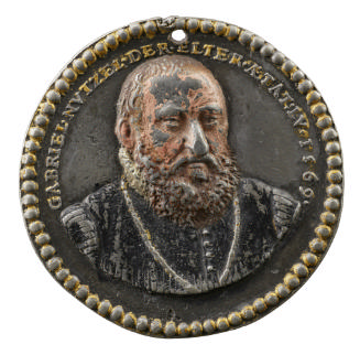 Polychrome lead medal of a man with short hair, a mustache and a beard, wearing a coat and chai…