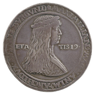 Silver medal of a man with long hair and crowned with a wreath