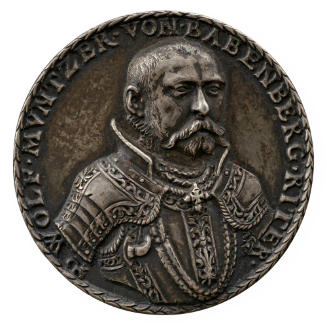 Silver medal of man with beard and mustache, wearing decorative armor and a chain with pendant