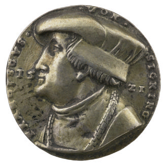 Silver medal of a man in profile to the left wearing a hat, cloak and chain