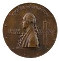 Bronze medal of a man in profile to the left with hair in a ponytail, wearing a jacket over a r…