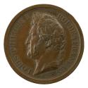 Bronze medal of a man in profile to the left wearing a wreath of laurels