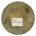 Unmarked tin reverse of a medal with a white rectangular sticker just below the center, on whic…