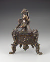 Alternate view of a bronze triangular lamp with a seated satyr who has his arms behind him.  He…