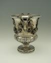 Silver wine cooler with intricate plant designs and rams' heads, side view