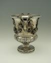 Silver wine cooler with intricate plant designs and rams' heads, side view