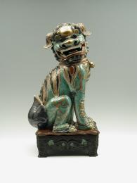 Green porcelain lion gold, black, and red stylized markings, seated on hind legs, on a black ba…