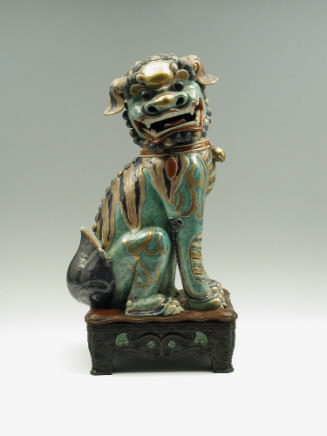 Green porcelain lion gold, black, and red stylized markings, seated on hind legs, on a black ba…