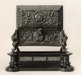 Bronze casket with protruding head in the middle at the back and various intricate motifs throu…