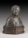 A bronze reliquary bust of a female saint.  Her head is tilted to her left and her eyes are clo…