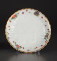 White saucer with raised swan motif in white at the center.  Painted floral motif and a blue cr…