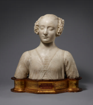 A marble bust of a young woman.  Her hair is parted in the middle and her curly hair is bound u…