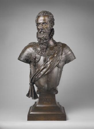 A bronze sculpture of a male subject looking straight ahead, he has curly hair and a long wavy …